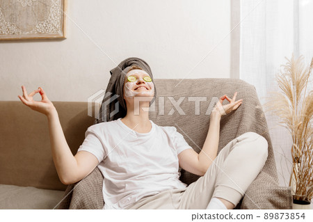 Young woman with casual clothes, towel on head and beauty mask on face sitting on couch and resting. Relax after taking shower. Cosmetic for women, skin care. Self care, time for yourself. Relaxing, Young woman with casual clothes, towel on head and beauty mask on face sitting on couch and resting. Relax after taking shower. Cosmetic for women, skin care. Self care, time for yourself. Relaxing, 89873854