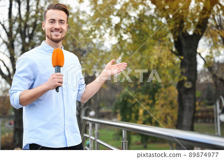 Young male journalist with microphone working in park. Space for text 89874977