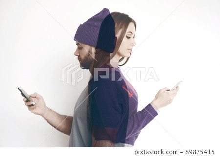 Portrait of young modern couple standing back to back and using smartphones on white background, double exposure Portrait of young modern couple standing back to back and using smartphones on white background, double exposure 89875415