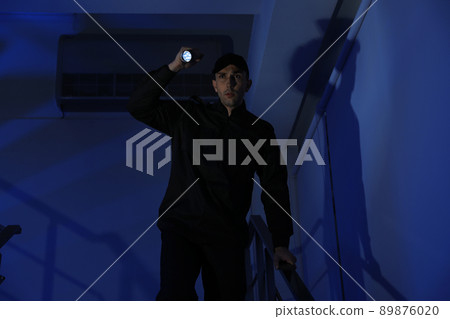 Male security guard with flashlight on stairs in darkness Male security guard with flashlight on stairs in darkness 89876020