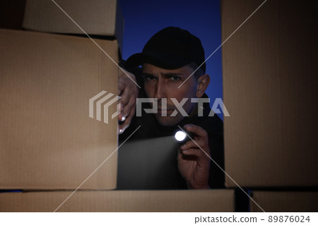 Security guard with flashlight looking through pile of cardboard boxes in dark room Security guard with flashlight looking through pile of cardboard boxes in dark room 89876024