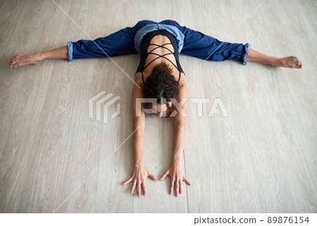 High angle view of young curly woman practicing splits on wooden floor in dancing studio 89876154