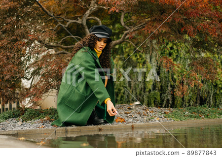 Under the tree with purple leaves at the backwater crouched a girl in autumn clothes and lets into the water autumn leaves Under the tree with purple leaves at the backwater crouched a girl in autumn clothes and lets into the water autumn leaves 89877843