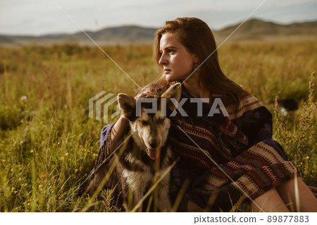 a girl in an ethno cape sits on the steppe grass hugging the dog's hand a girl in an ethno cape sits on the steppe grass hugging the dog's hand 89877883