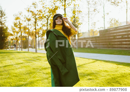 bright green grass in the park on which stands a cheerful girl in a bright sweater throwing a coat on one shoulder bright green grass in the park on which stands a cheerful girl in a bright sweater throwing a coat on one shoulder 89877908