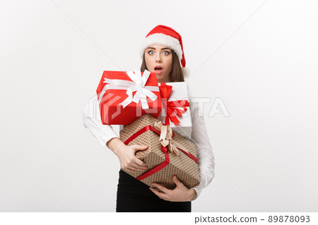 Business Concept - Beautiful young caucasian business woman with santa hat holding a lot of gift boxes with surprising facial expression. Business Concept - Beautiful young caucasian business woman with santa hat holding a lot of gift boxes with surprising facial expression. 89878093