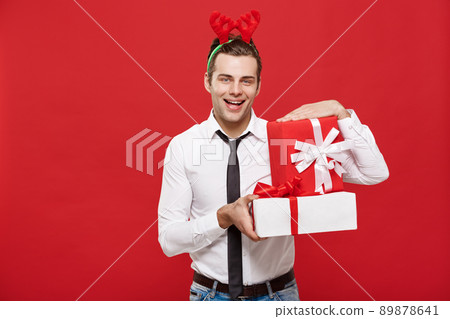 Christmas Concept - Cheerful happy young businessman with a decorative gift isolated on red background. 89878641