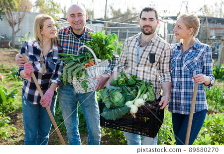 Family of four professional gardeners holding harvest of vegetables and greens 89880270