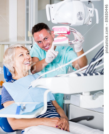 young male dentist explaining future treatment to female patient on dental model 89880446