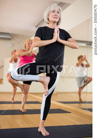 Group of aged women standing in tree pose Group of aged women standing in tree pose 89880476