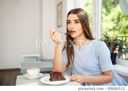 Young attractive Caucasian lady enjoy eating chocolate cake with hot coffee in modern coffee shop at noon. Young attractive Caucasian lady enjoy eating chocolate cake with hot coffee in modern coffee shop at noon. 89880512