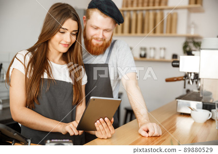 Coffee Business Concept - Satisfied and smile owners couple look on tablet orders online in modern coffee shop 89880529