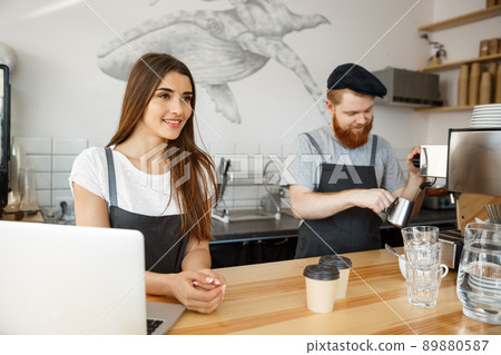 Coffee Business Concept - Positive young bearded man and beautiful attractive lady barista couple enjoy working together at the modern coffee shop Coffee Business Concept - Positive young bearded man and beautiful attractive lady barista couple enjoy working together at the modern coffee shop 89880587