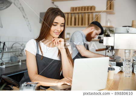 Coffee Business Concept - beautiful caucasian bartender barista or manager working and planing in laptop at modern coffee shop. Coffee Business Concept - beautiful caucasian bartender barista or manager working and planing in laptop at modern coffee shop. 89880610