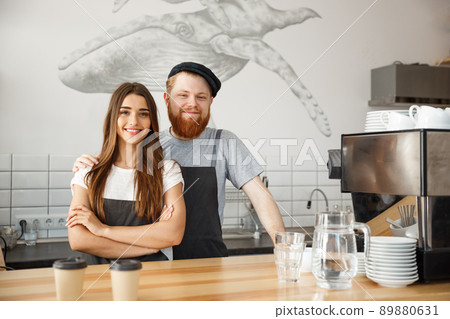 Coffee Business Concept - Positive young bearded man and beautiful attractive lady barista couple enjoy working together at the modern coffee shop 89880631