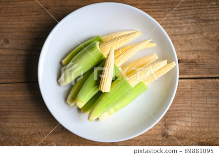 Baby corn on white plate, Fresh young baby corn for cooking health food, Close up raw organic baby corn on wooden background. 89881095