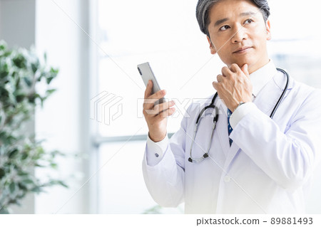 A doctor in a white coat standing by the window with a smartphone 89881493