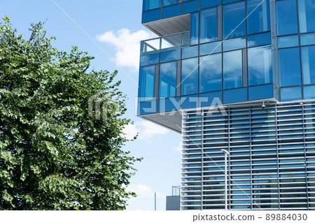 a building with mirrored windows next to a green tree, Against the background of a blue sky 89884030