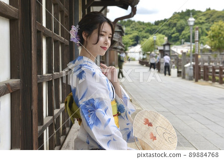 一位身著浴衣的年輕女子，在小江戶佐原的街道上微笑著，手裡拿著一把扇子 89884768