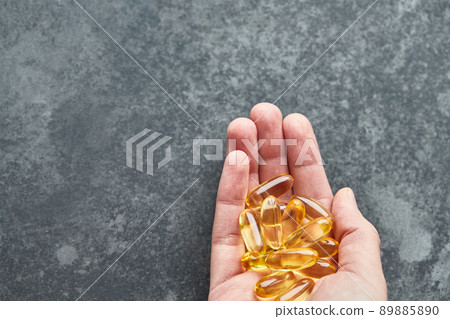 A person holds an omega-3 fatty acid capsule against a gray background. The concept of medicine and healthy living. Top view. 89885890