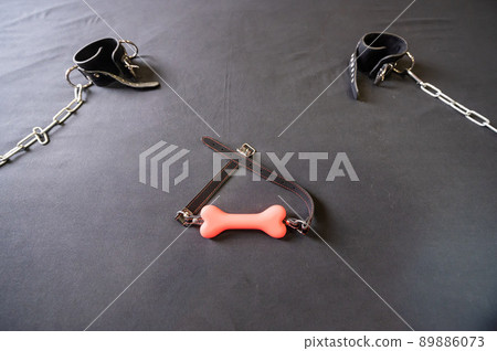 A bone-shaped gag and leather handcuffs with chains on a gray sheet. BDSM concept. Role-playing games for adults. Domination and obedience. A bone-shaped gag and leather handcuffs with chains on a gray sheet. BDSM concept. Role-playing games for adults. Domination and obedience. 89886073