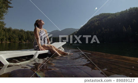Woman lie on a sunbed in sunglasses and a boho silk shawl. Girl rest on a flood wood underwater pier. The pavement is covered with water in the lake. Woman lie on a sunbed in sunglasses and a boho silk shawl. Girl rest on a flood wood underwater pier. The pavement is covered with water in the lake. 89889127