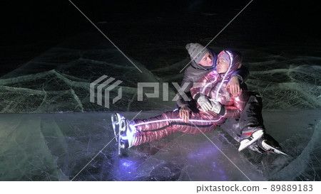 Young loving couple skating at ice rink at night. Man and woman kiss hug have fun learn to skate. Making love on ice. Ice illuminated backlit below. Young loving couple skating at ice rink at night. Man and woman kiss hug have fun learn to skate. Making love on ice. Ice illuminated backlit below. 89889183