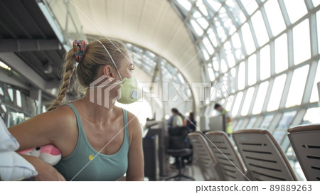 Woman caucasian at airport with wearing protective medical mask on head against the background of the plane. Coronavirus sars-cov-2 covid-19. 89889263