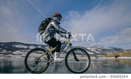 Woman is riding bicycle on the ice. Tires on bike are covered wi Woman is riding bicycle on the ice. Tires on bike are covered wi 89889264