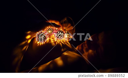 Magic hot light from lanterns falls on the woman eyes. The naked adult sexy caucasian girl lies at night on the bed and holds warm lamps in her hands. Magic hot light from lanterns falls on the woman eyes. The naked adult sexy caucasian girl lies at night on the bed and holds warm lamps in her hands. 89889352