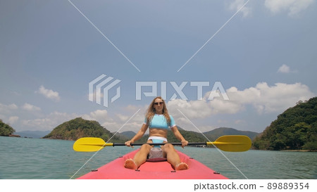 Sportive woman rows pink plastic canoe along sea water. Positive sports girl hand padding on kayak, front view. 89889354