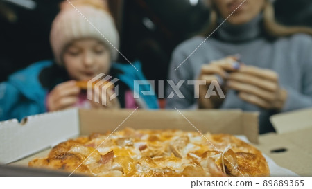 Mother and daughter eat pizza cheese four. Close up of young woman eating pizza and chewing in outdoor restaurant. Girl hands taking pieces pizza. 89889365