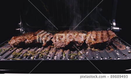 Delicious juicy meat steak cooking on grill. Prime beef fry on electric roaster, rosemary, black pepper, salt. Slow motion. Delicious juicy meat steak cooking on grill. Prime beef fry on electric roaster, rosemary, black pepper, salt. Slow motion. 89889493