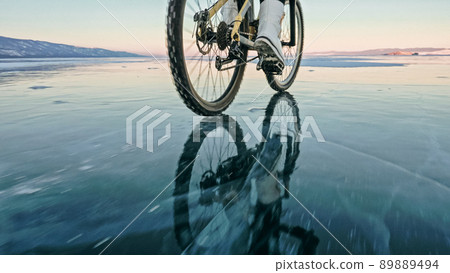 Woman is riding bicycle on the ice. Tires on bike are covered wi 89889494