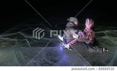 Young loving couple skating at ice rink at night. Man and woman kiss hug have fun learn to skate. Making love on ice. Ice illuminated backlit below. 89889516