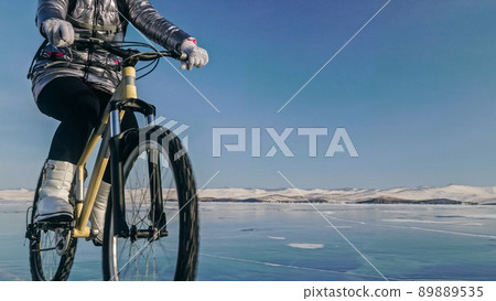 Woman is riding bicycle on the ice. Tires on bike are covered wi Woman is riding bicycle on the ice. Tires on bike are covered wi 89889535