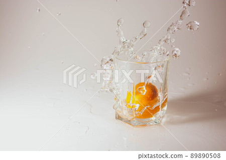 Orange mandarin drops in a glass with water on a cream background drops and splashes of water 89890508