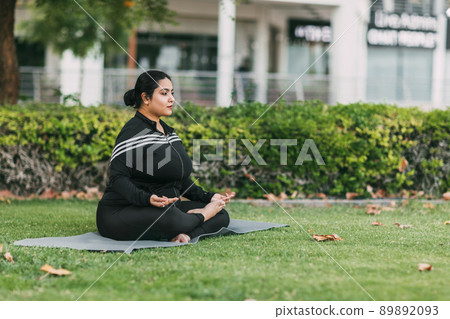 An Indian woman practices yoga and meditation in the lotus asana pose in an outdoor summer park. Side view. 89892093