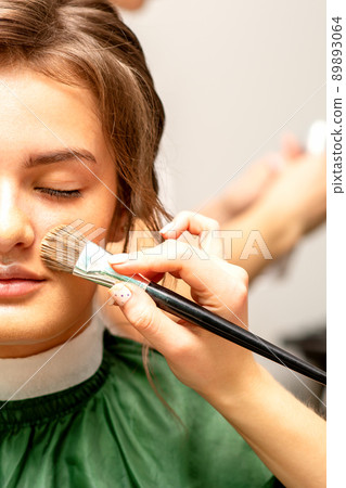 The makeup artist applies a cosmetic tonal foundation on the face using a makeup brush 89893064