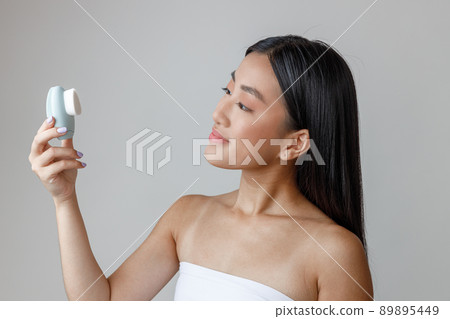 Asian young woman holding face massager cleansing device Asian young woman holding face massager cleansing device 89895449