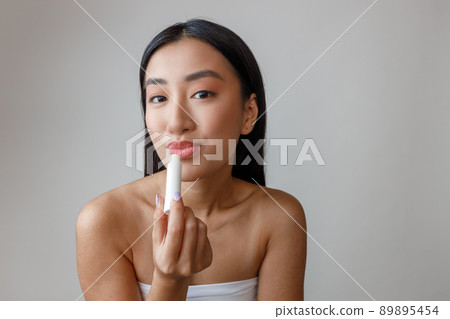 Asian young woman using hygienic lipstick in studio Asian young woman using hygienic lipstick in studio 89895454