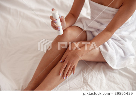 Young woman applying cosmetic cream on leg after taking bath Young woman applying cosmetic cream on leg after taking bath 89895459