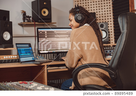 African cute woman blogger records online podcast using laptop, headphones and microphone in professional music studio 89895489