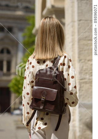 Part photo of a woman with a brown leather backpack with antique and retro look. Outdoors photo 89896071