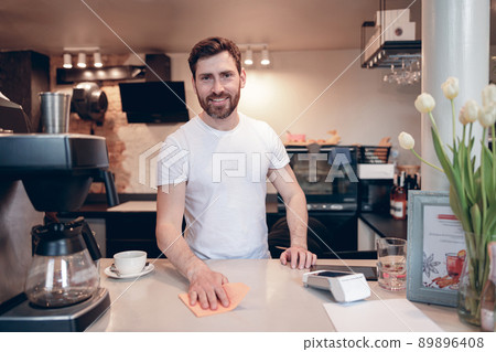 Handsome Caucasian happy male bartender cleaning counter and smiling to camera. Cafe job. 89896408