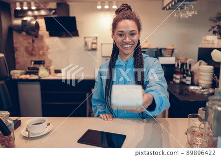 Mixed-races young pretty female barista handing paying terminal to client. Cashless paying. 89896422