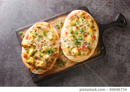 German pizza style tart flambee Swabian Dinnete with potatoes, onions and bacon close-up on a wooden board. horizontal top view German pizza style tart flambee Swabian Dinnete with potatoes, onions and bacon close-up on a wooden board. horizontal top view 89896734
