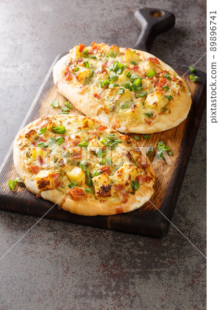 Dinnete is a traditional German dish originating from Baden-Wurttemberg is topped with sour cream, potatoes, onions, ham, and cheese close-up on a wooden board. vertical Dinnete is a traditional German dish originating from Baden-Wurttemberg is topped with sour cream, potatoes, onions, ham, and cheese close-up on a wooden board. vertical 89896741