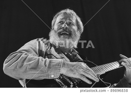 Bottom view of stylish senior bearded man, rock musician playing guitar isolated on dark background. Rehearsal base Concept of art, music, style, older generation, vintage 89896838