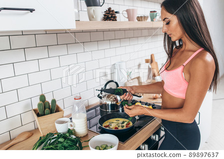 Sporty woman holding frying pan and mixing omlete Sporty woman holding frying pan and mixing omlete 89897637